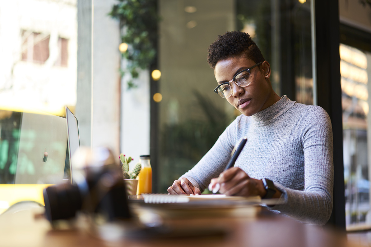 A woman making notes beside a laptop