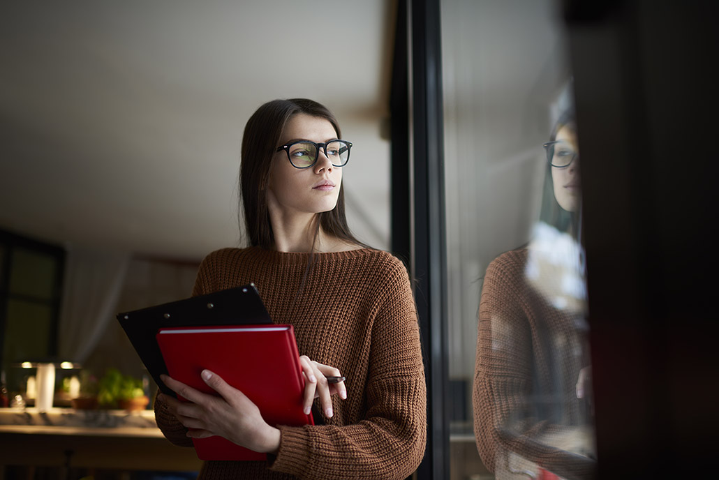 A student holding books and looking out of a university window